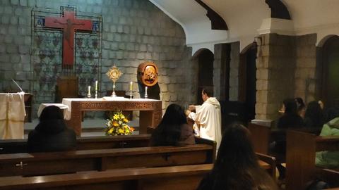 Una ceremonia religiosa en una iglesia con un altar, un sacerdote y varias personas sentadas.
