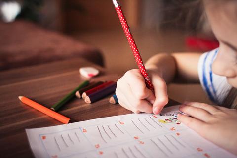 Un niño está escribiendo en una hoja con lápices de colores alrededor.