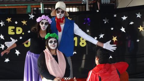 Un grupo de personas disfrazadas con maquillaje de calavera y trajes coloridos se presentan en un escenario decorado con estrellas y un fondo negro.