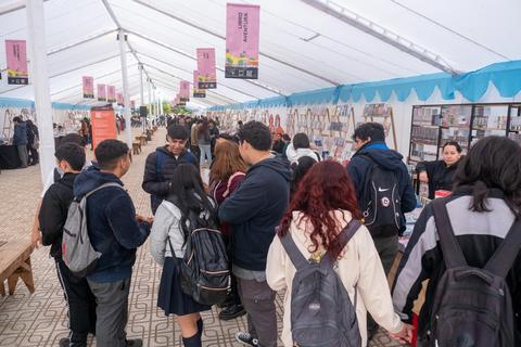 Un grupo de estudiantes se reúne en un espacio cubierto con mesas y carteles en una feria.
