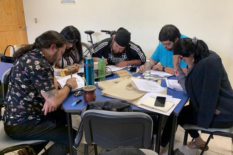 Un grupo de personas se reúne en una mesa para trabajar en conjunto en sus tareas.