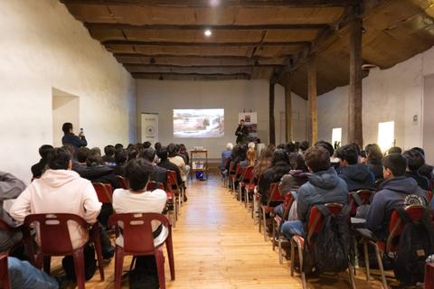 Una sala llena de asistentes en un evento donde se proyecta una presentación.