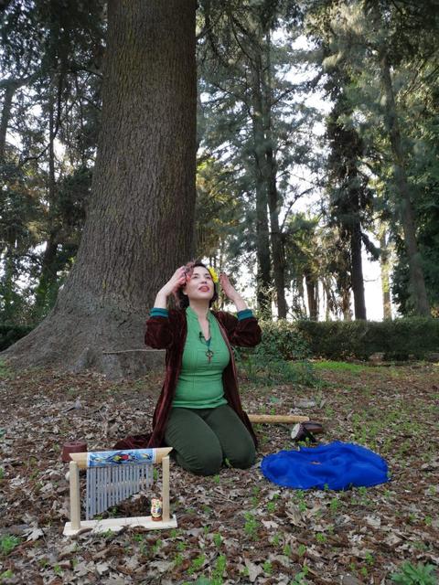Una mujer se encuentra de rodillas en un bosque, con las manos en la cabeza, rodeada de naturaleza.