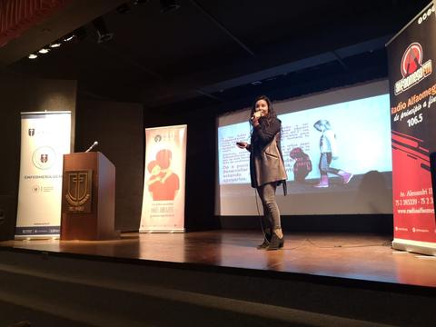 Una mujer presenta en una conferencia mientras una proyección se muestra detrás de ella.