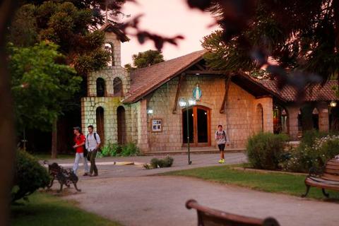 Una escena en un parque al atardecer, con personas caminando junto a un edificio de piedra.