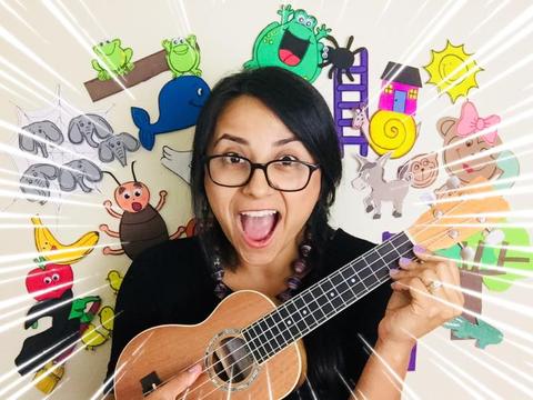 Una mujer sonriente sostiene un ukelele frente a una colorida pared decorada con dibujos infantiles.
