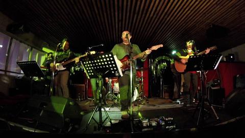 Una banda de música toca en un escenario iluminado en un local.