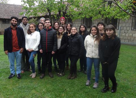 Un grupo de personas de pie en un jardín, vistiendo ropa de abrigo en un día nublado.
