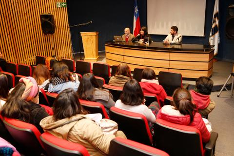 Una conferencia en un auditorio con un panel de tres personas hablando frente a una audiencia.