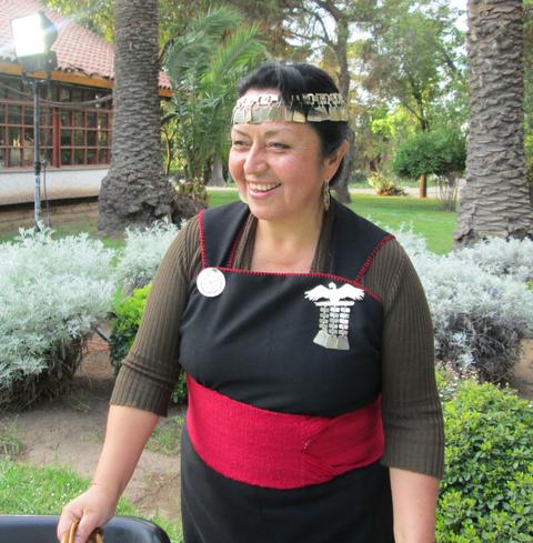 Mujer sonriente vestida con atuendo tradicional, en un entorno natural con plantas y árboles.