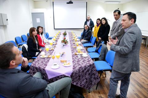 Un grupo de personas está reunido alrededor de una mesa en un entorno profesional, mientras uno de ellos habla con gestos.