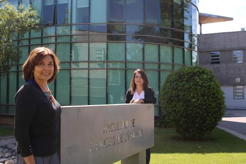 Dos mujeres posan frente a un edificio de la Facultad de Ciencias de la Salud.