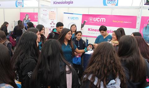 Un grupo de estudiantes se agrupa en un stand informativo sobre Kinesiología en un evento académico.