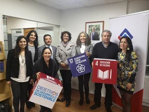 Un grupo de personas posando con carteles que representan los Objetivos de Desarrollo Sostenible en una oficina.