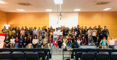 Una gran reunión de un grupo diverso de personas posando para la foto en un auditorio.