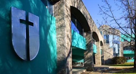 Edificio con una fachada moderna y un logo en forma de escudo con una cruz.