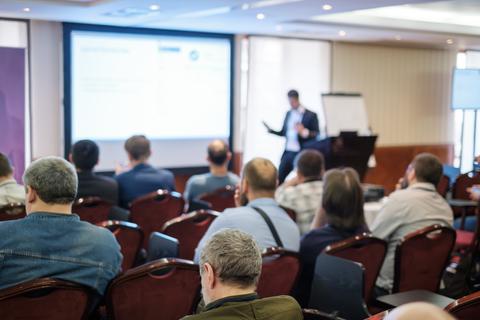 Una presentación en una sala de conferencias con un ponente frente a una audiencia.