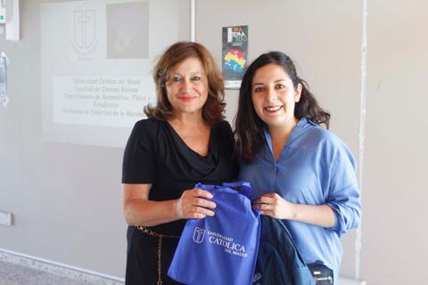 Dos mujeres sonríen mientras sostienen bolsas de la Universidad Católica del Maule en un ambiente académico.