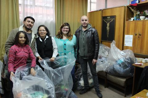 Un grupo de cinco personas se encuentra en una sala, posando con bolsas de plástico tras haber recolectado donaciones.
