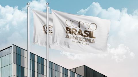Una imagen que muestra las banderas de la COP30 en Brasil con un fondo de nubes y un edificio moderno.