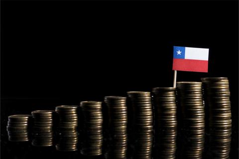 La imagen muestra pilas de monedas con una bandera de Chile en la parte superior de una de ellas.