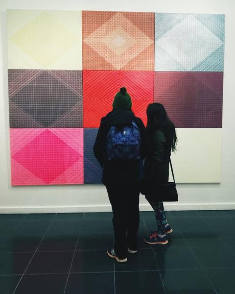 Dos personas observan una obra de arte compuesta por cuadrados de diferentes colores y patrones.