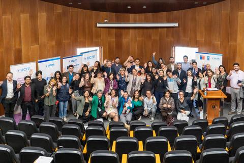Grupo de personas reunidas en un auditorio, sonriendo y saludando a la cámara.