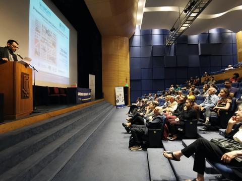Un ponente presenta en un auditorio a un público atento durante un evento.
