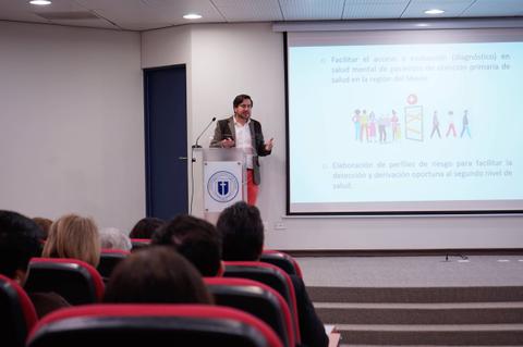 Un presentador habla sobre el acceso a la salud ante una audiencia en una sala de conferencias.