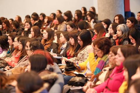 Una gran multitud de mujeres sentadas en un auditorio, prestando atención a una presentación.