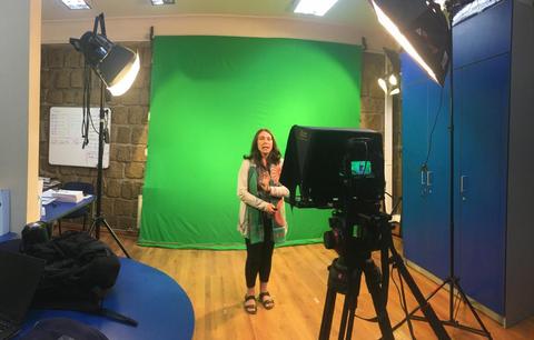 Una mujer está de pie frente a una pantalla verde en un estudio de grabación.