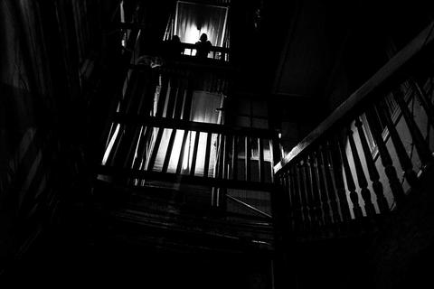 Una escalera oscura con iluminación tenue y una figura en la parte superior.