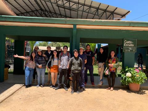 Un grupo de personas sonrientes se encuentra en la entrada de una escuela.