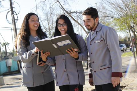 Tres jóvenes estudiantes revisan un cuaderno en un ambiente exterior.