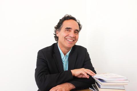 Un hombre sonriente está sentado frente a una mesa con varios libros apilados.