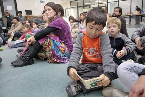 Un grupo de personas, incluyendo niños, se reúne en un ambiente interior para disfrutar de una actividad de lectura.