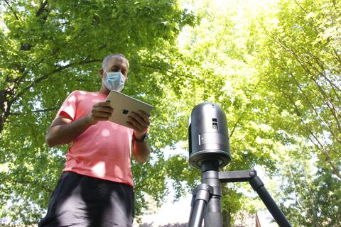 Un hombre con mascarilla está usando una tableta mientras observa un dispositivo en un entorno natural.