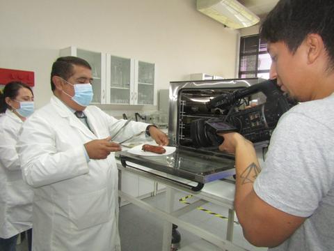 Un grupo de personas en un laboratorio observan cómo un hombre corta un objeto mientras es grabado con una cámara.