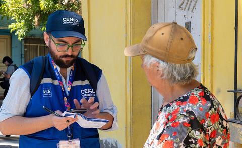 Un encuestador conversa con una mujer mayor en la calle mientras toma notas.