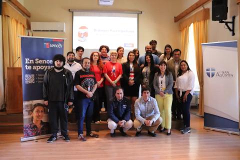 Grupo de personas posando en un evento con banners de Sence y San Agustín.