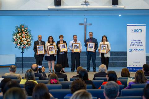 Un grupo de personas sostiene marcos con fotografías en un evento celebrado en un auditorio decorado con flores y una cruz en la pared.