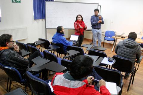 Un grupo de personas asiste a una clase con un par de instructores que presentan un tema en una pizarra.