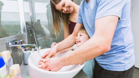 Una familia sonriente se lava las manos juntos en un lavabo.
