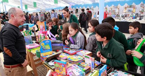 Un grupo de niños observa con atención a un vendedor en una feria de libros y materiales escolares.