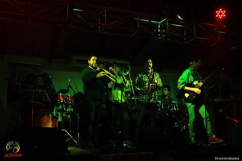 Una banda de música toca en un escenario iluminado con luces verdes y rojas.