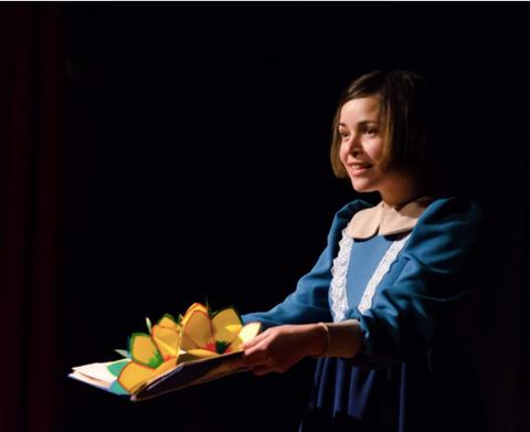 Una joven dedicada a la narración de cuentos sostiene un libro pop-up colorido en un escenario oscuro.