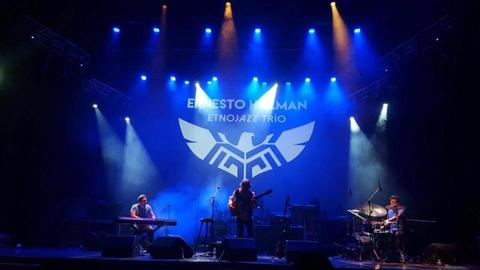 Una actuación musical en un escenario con iluminación colorida y un trío de músicos tocando instrumentos.