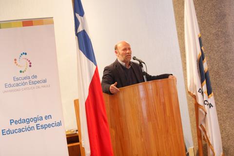 Un hombre habla en un podio frente a una bandera chilena en un evento educativo.