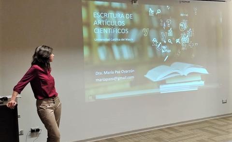 Una mujer presenta un tema sobre la escritura de artículos científicos frente a una audiencia.