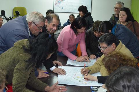 Un grupo de personas se reúne alrededor de una mesa, colaborando en un plano o mapa.